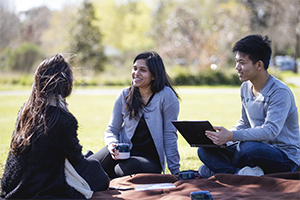 Three students sitting together in a park, enjoying a relaxed moment — as featured in our latest news article.